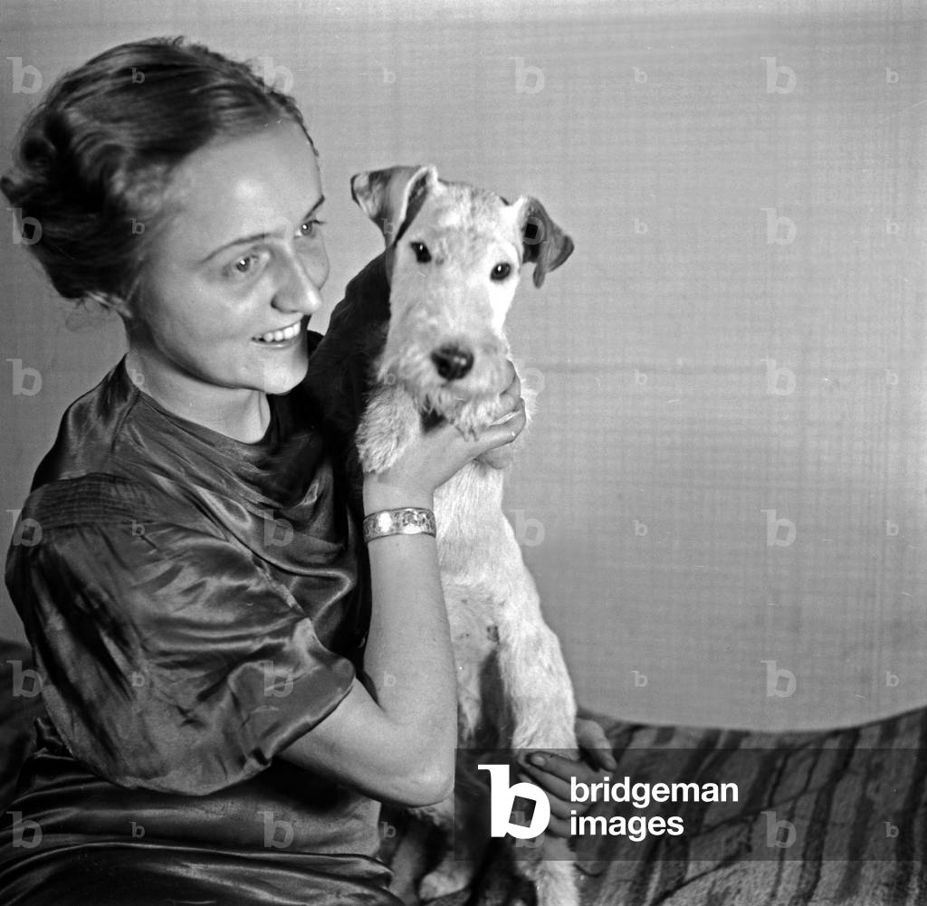 A lady and her dog pet at the photo studio in contemporary fashion, Germany 1930s (b/w photo)