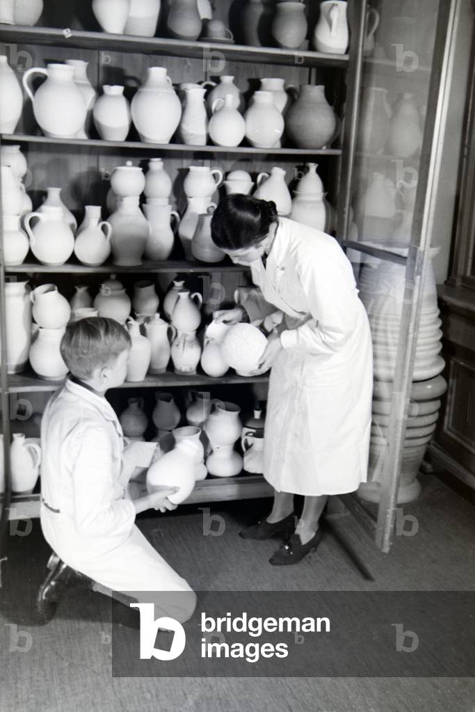 Students of the College for Ceramics in front of a big cupboard filled with ceramics, Höhr-Grenzhausen, Germany 1930s (b/w photo)