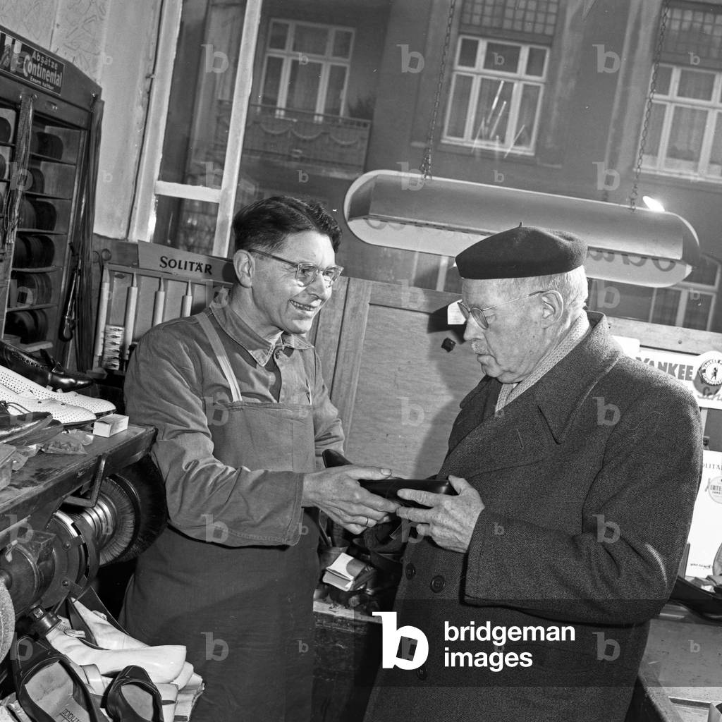 An elder man taking a pair of shoes from the shoemaker, Germany 1960s