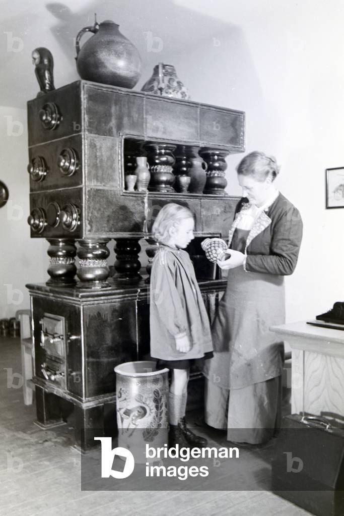 A master potter is showing a finished stoneware jug to a little girl, Germany 1930s (b/w photo)