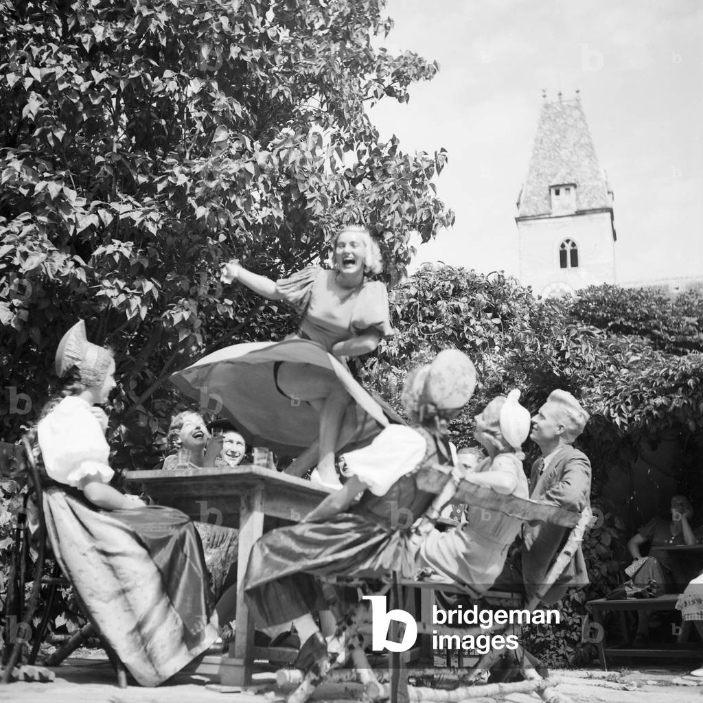 A young woman tasting the wine of the Wachau area in Austria and dancing on the table, Germany 1930s (b/w photo)