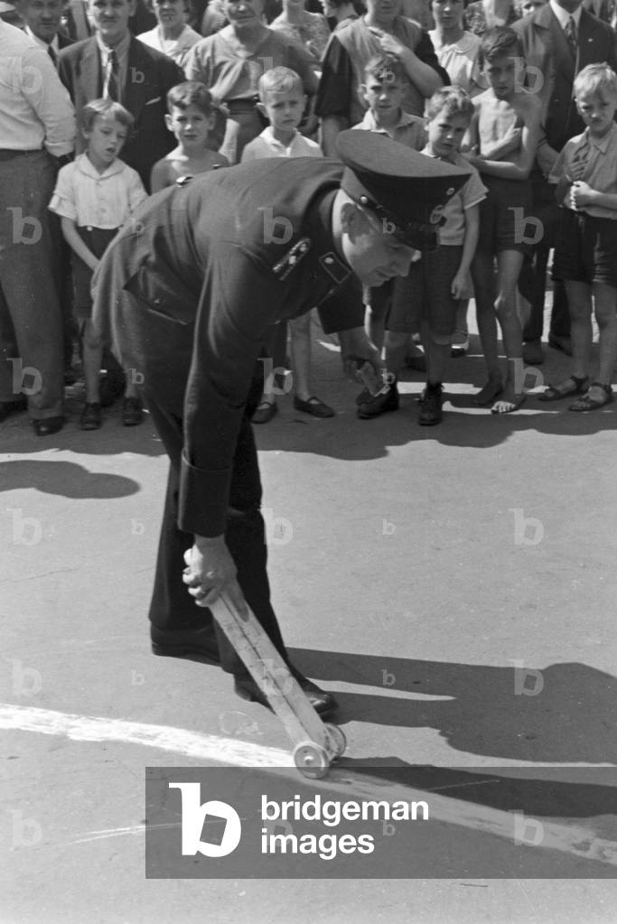 A policeman strewing chalk to a petrol track at a traffic accident, Germany 1930s (b/w photo)