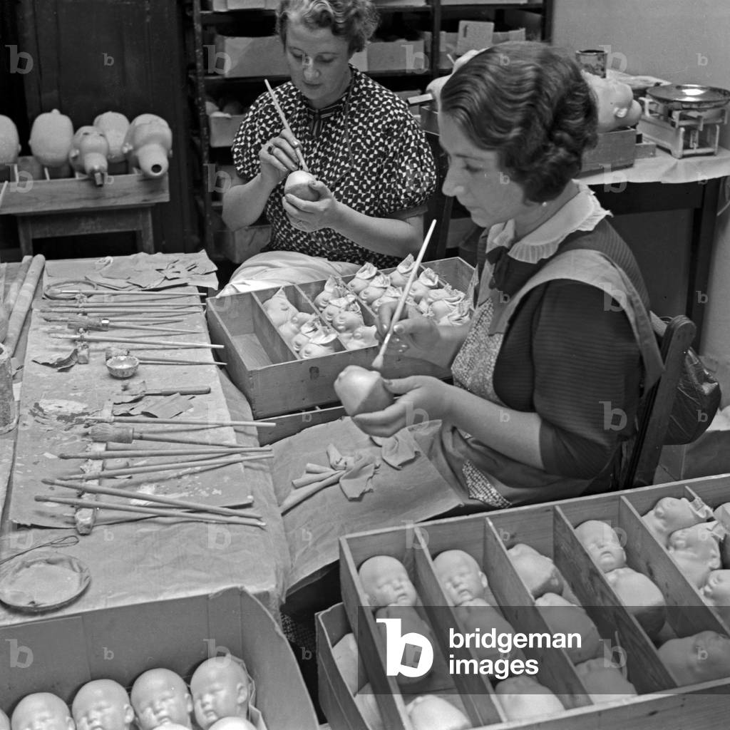 Female staff members of the Kaethe Kruse doll factory painting the porcellain heads, Germany 1930s (b/w photo)