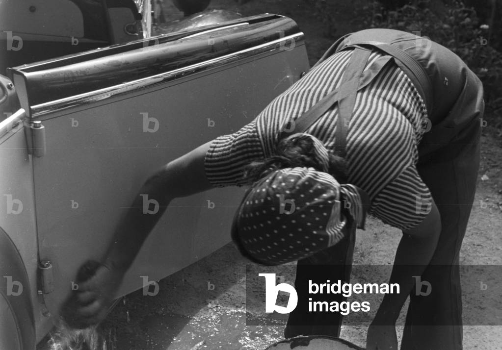 A young woman washing a Ford model Eifel, Germany 1930s (b/w photo)