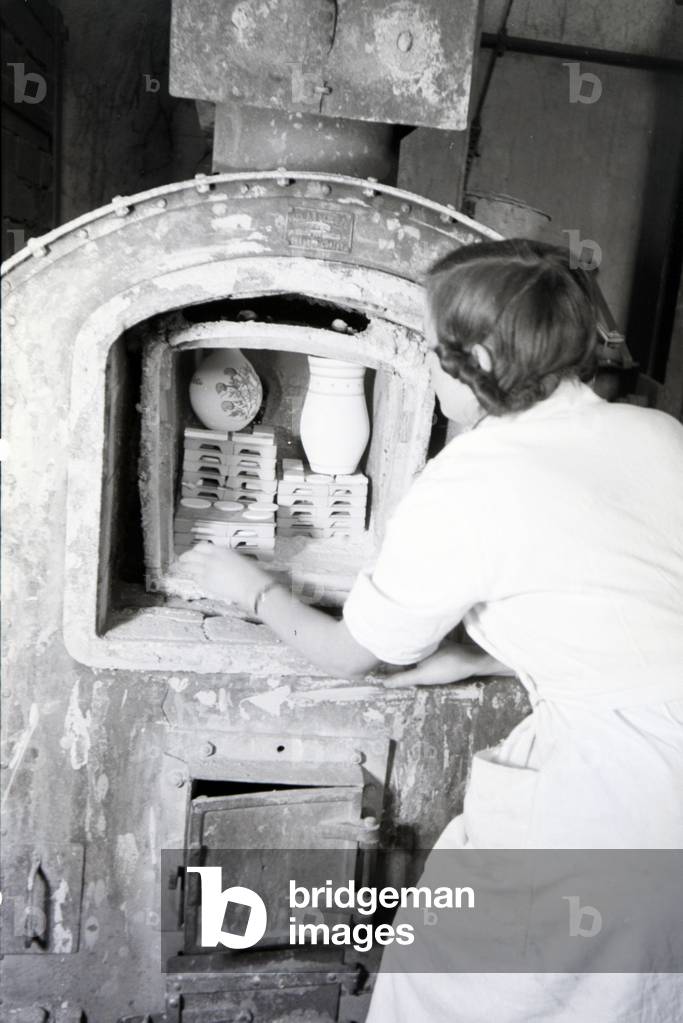 A student of the College for Ceramics is putting newly fictiled vases into the kiln, Höhr-Grenzhausen, Germany 1930s (b/w photo)