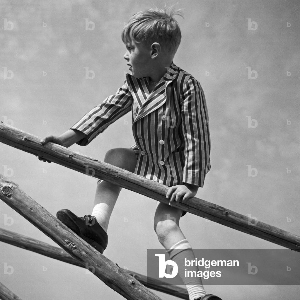 A little boy playing and climbing on a woodden framework, Germany 1930s (b/w photo)