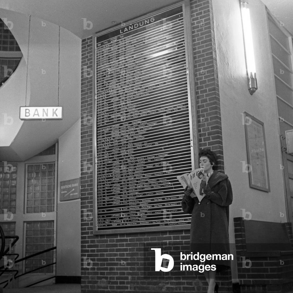 German schlager singer Melitta Berg with a Burda magazine at the destination board of Hamburg airport, Germany 1950s