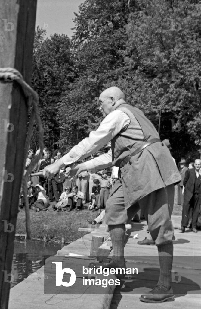 Old professional fisherman fishing on the shore of a lake, Germany 1930s (b/w photo)