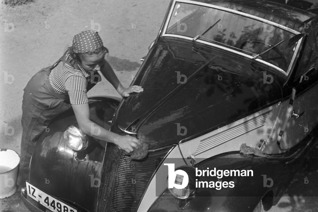 A young woman washing a Ford model Eifel, Germany 1930s (b/w photo)