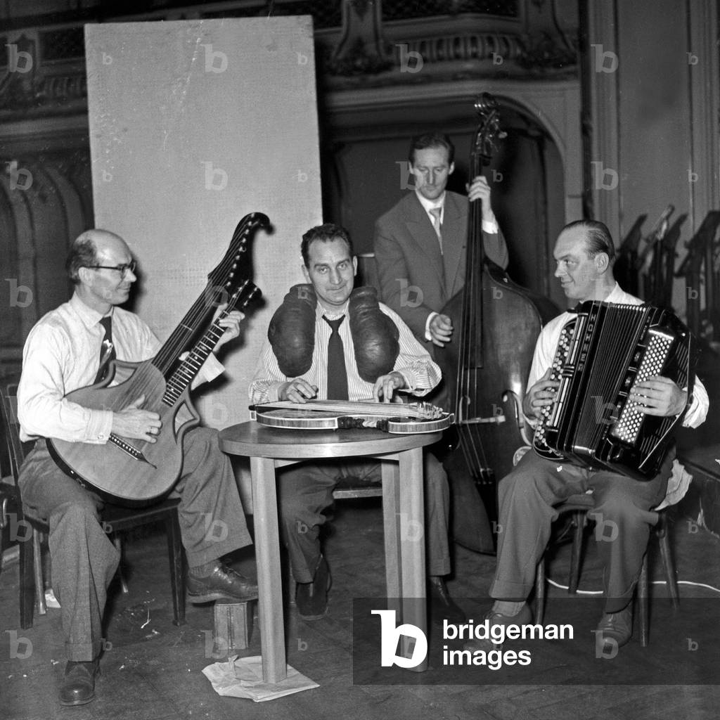 German composer and zither player Alfons Bauer with his instrument and boxing gloves accompanied by a small orchestra