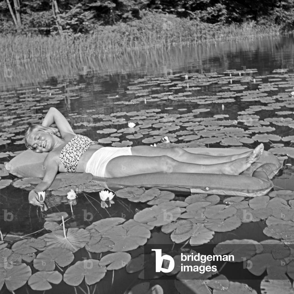 A young woman relaxing on an air mattress on a pond full of water lilies, Germany 1930s (b/w photo)