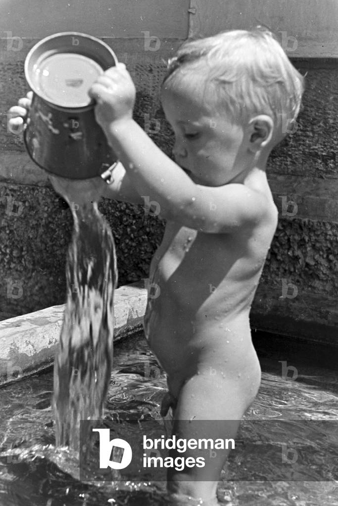 A playing toddler in the open-air swimming pool on a hot summer day, Germany 1930s (b/w photo)