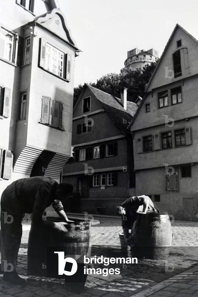Two men washing big wooden barrels on one of the streets of the historic district in Tübingen, Germany 1930s (b/w photo)