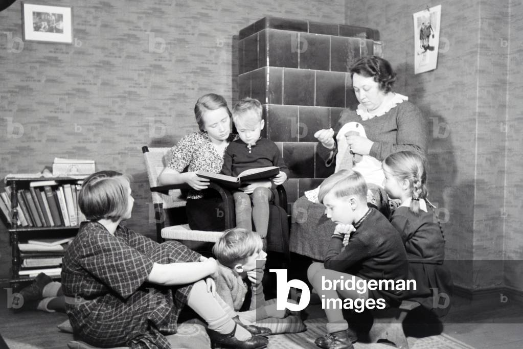 Members of a extended family reading a book together, Germany 1930s (b/w photo)