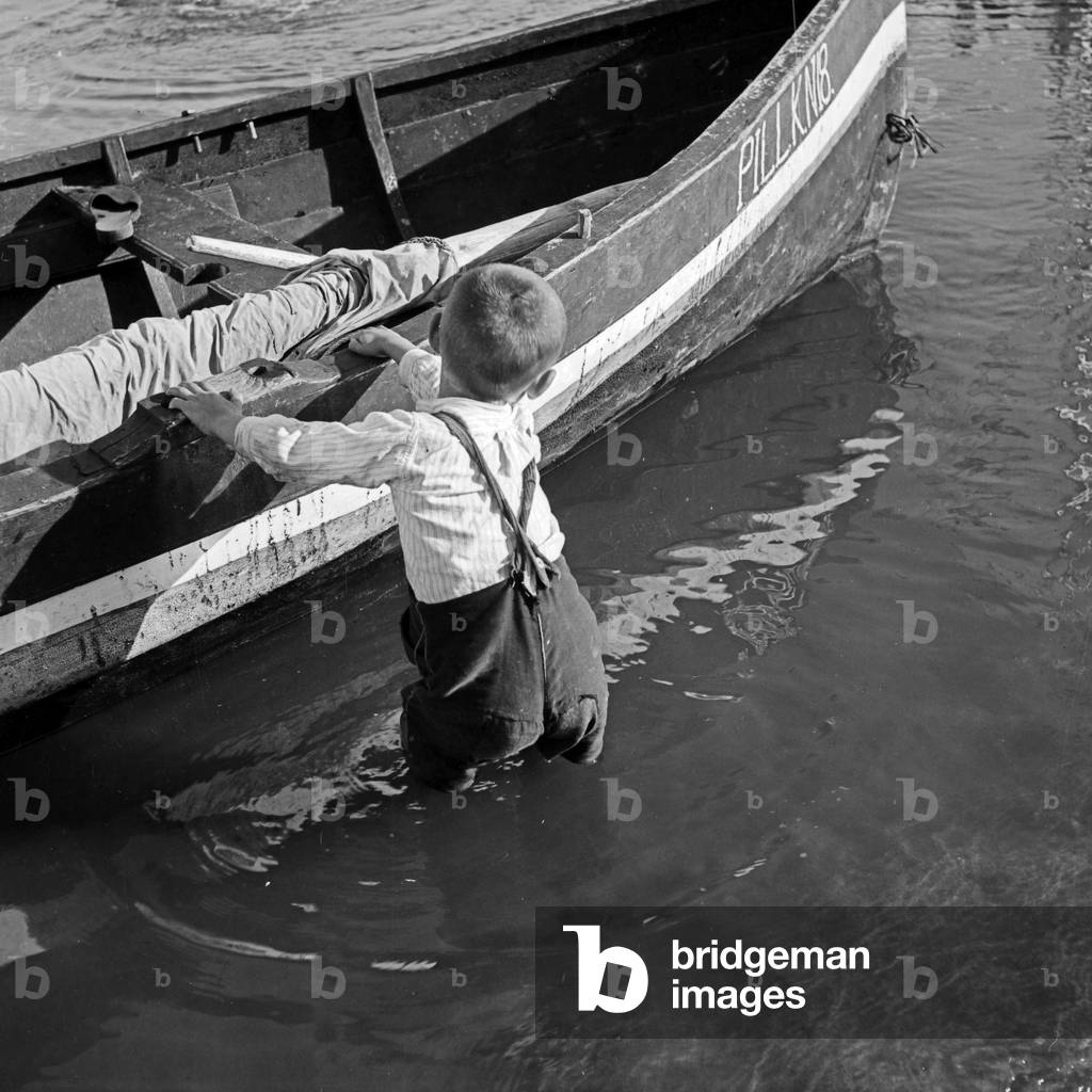 Little boy pulling a sailing boat to the shore near Pillkallen at Courland Split in East Prussia, Germany 1930s (b/w photo)