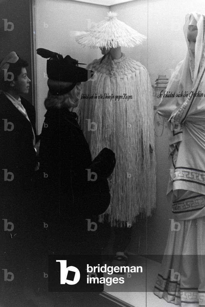 Visitors to a fair in front of a display case with Chinese and Greek costumes, on the occasion of the Wiener Modewoche in the house of fashion 