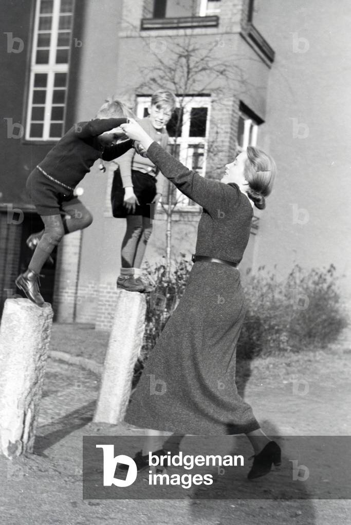 Members of an extended family playing in front of the apartment building , Germany 1930s (b/w photo)