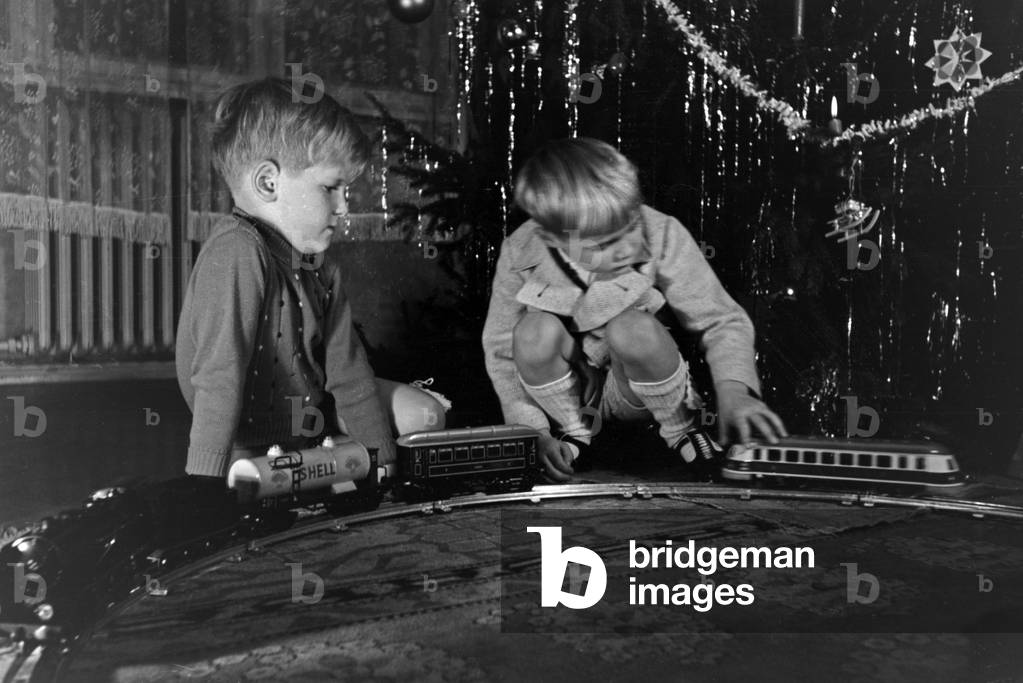 Two boys playing with the new model train under the christmas tree, Germany 1930s (b/w photo)