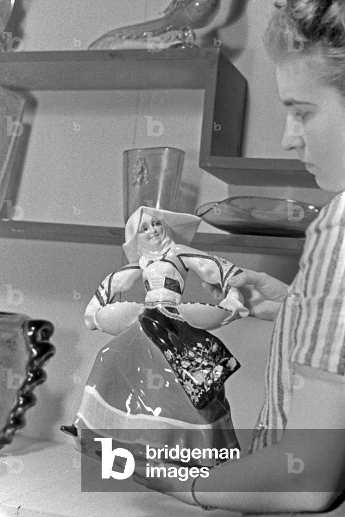 A female staff member at a booth for porcelain and ceramics with a statuette at the Leipzig trade show, Germany 1940s (b/w photo)