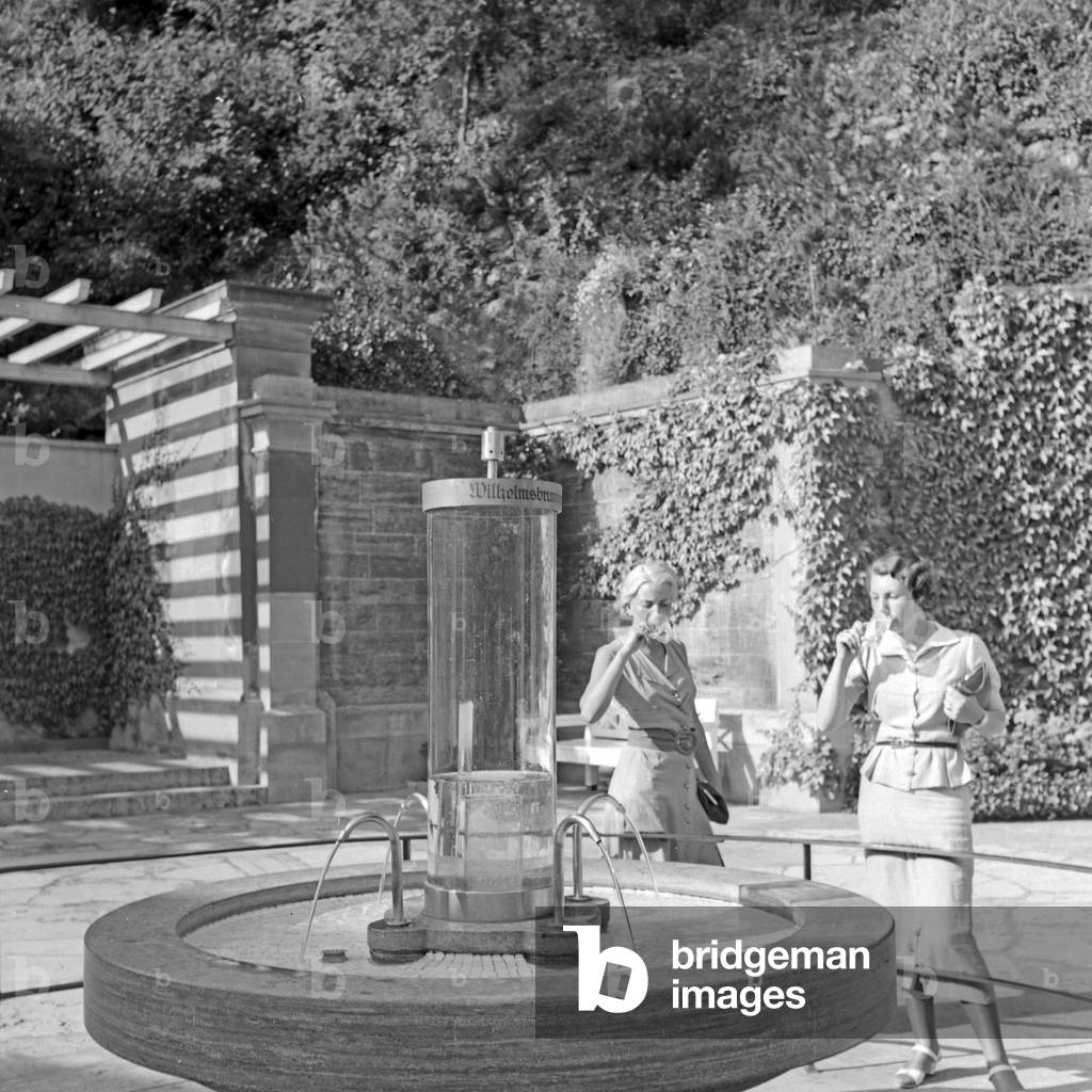 Two women drinking water from the Wilhelmsbrunnen well at Bad Cannstatt, Germany 1930s (b/w photo)