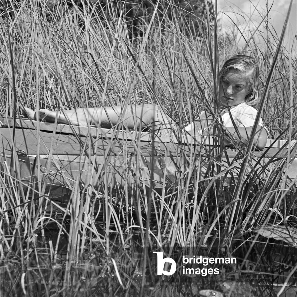 A young woman with her folding boat in the reed of a lake in the Wachau area, Germany 1930s (b/w photo)