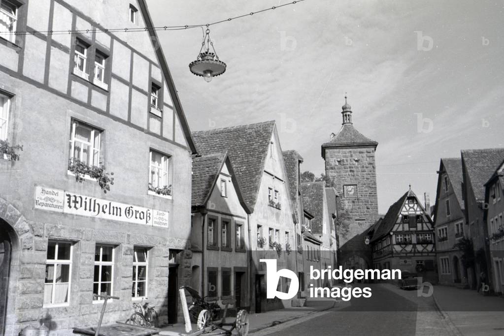 A paving stone alley leading toward the Sieberstor, Siebers Gate in Rothenburg ob der Tauber, past old carriages and half-timbered houses, Germany 1930s (b/w photo)