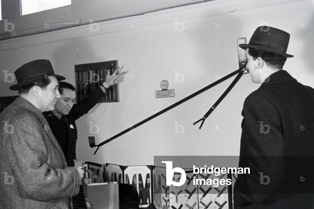 Visitors to a fair in front of a display case with suspenders by the Italian company Centenari e Zinelli S (b/w photo)