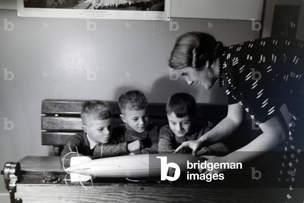 A teacher is explaining a zeppelin model to three school boys who are listening with great interest, zeppelin village near Frankfurt am Main, Germany 1930s (b/w photo)