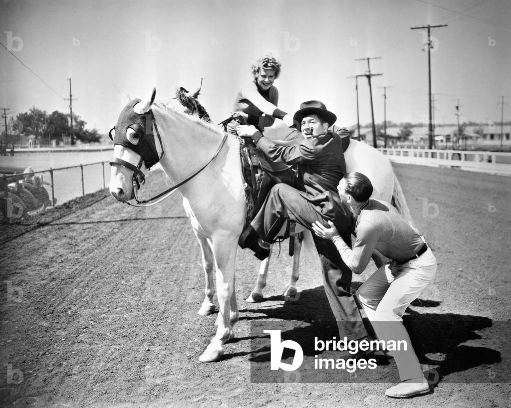 Young Couple Trying to Help a Man Get Onto his Horse
