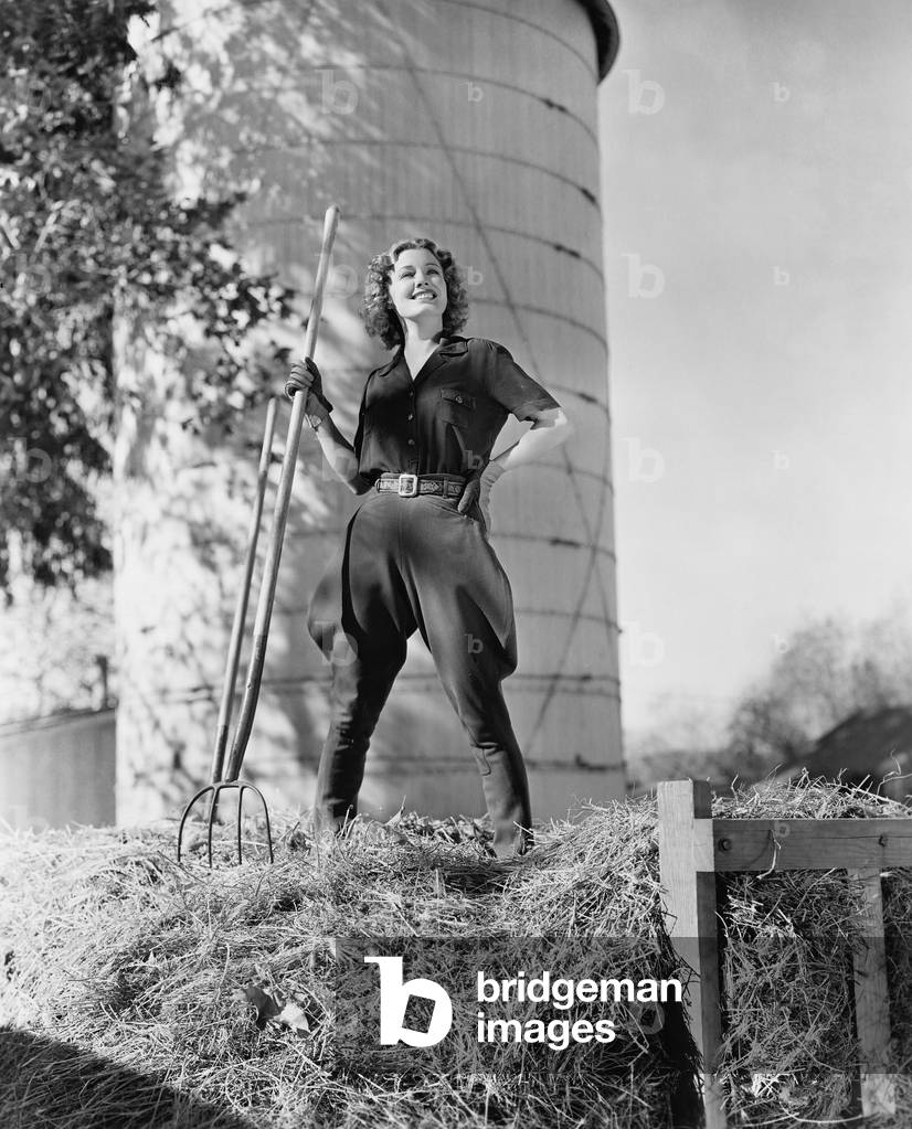 Young Woman Standing on a Haystack and Holding a Pitchfork