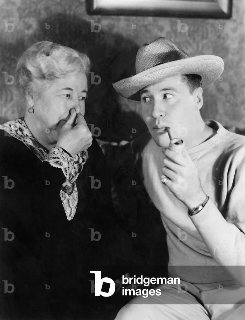 Young Man Smoking a Pipe with a Woman Holding her Nose