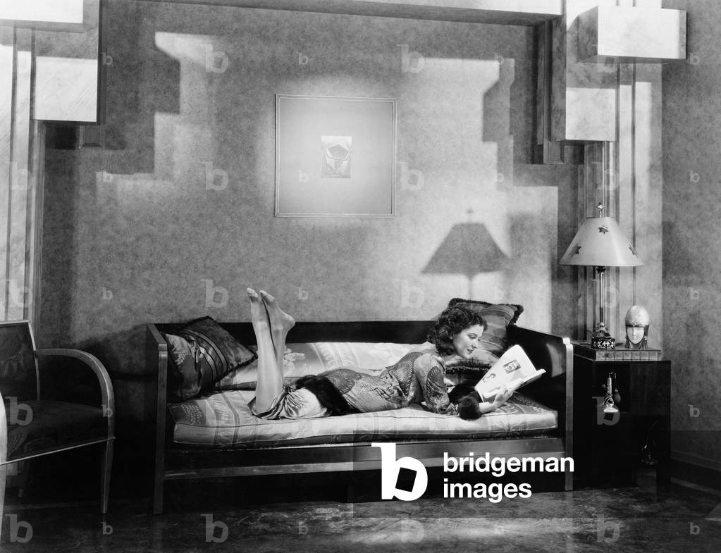 Young Woman Lying on a Couch and Reading a Magazine