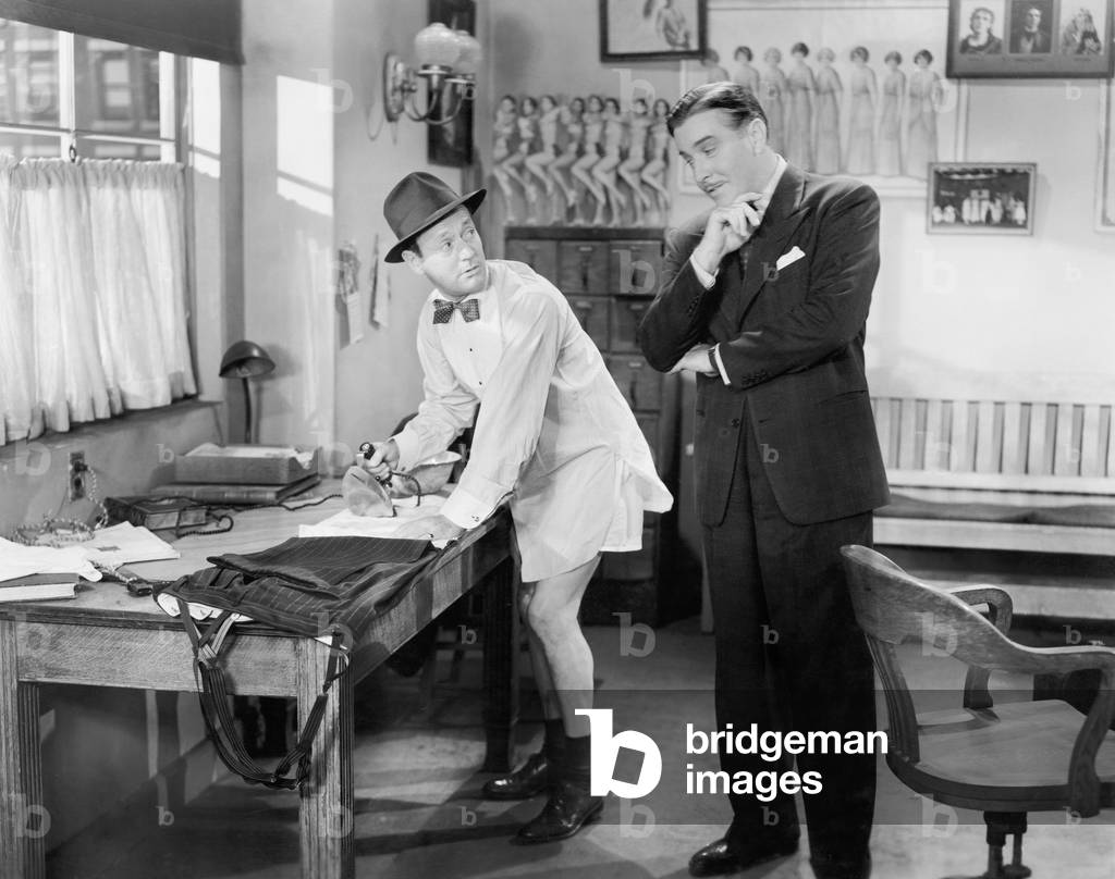 Two Men Standing in an Office, One Ironing his Pants