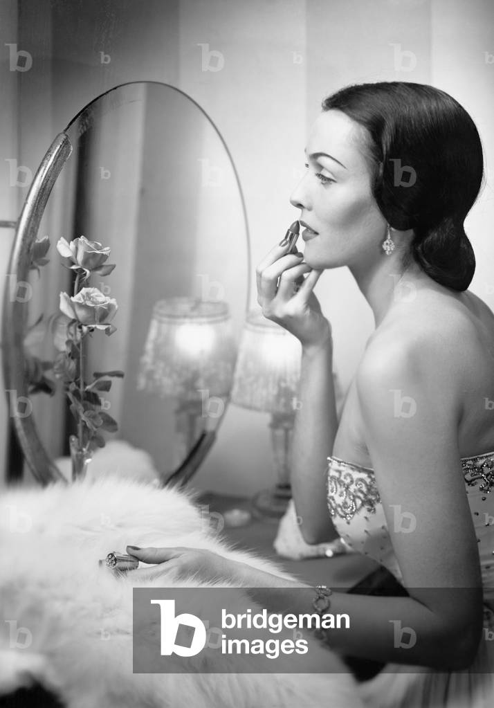 Young Woman Looking Into a Mirror and Putting on Make Up