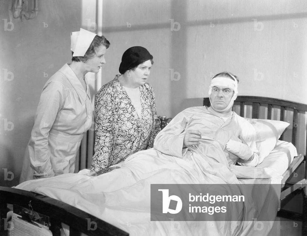 A Wife Next to her Husband in a Hospital Bed with a Nurse Attending