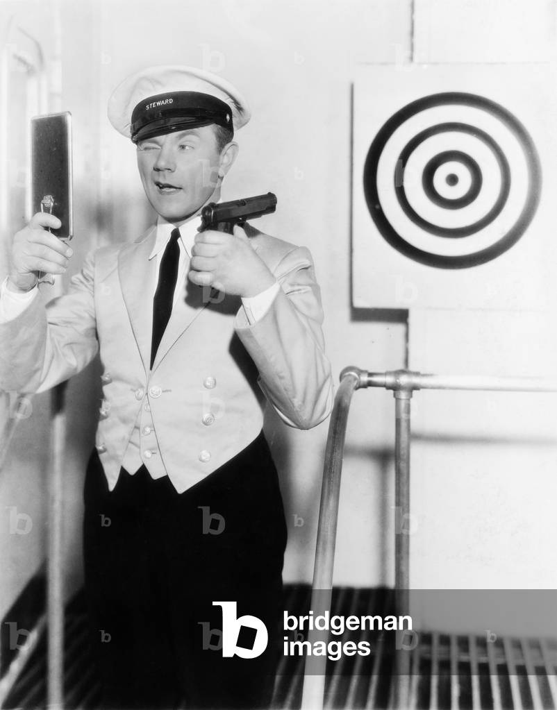 Young Man Looking at a Mirror and Aiming at a Dartboard with a Handgun