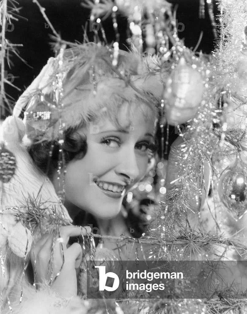 Young Woman Looking Through the Branches of a Christmas Tree with Ornaments