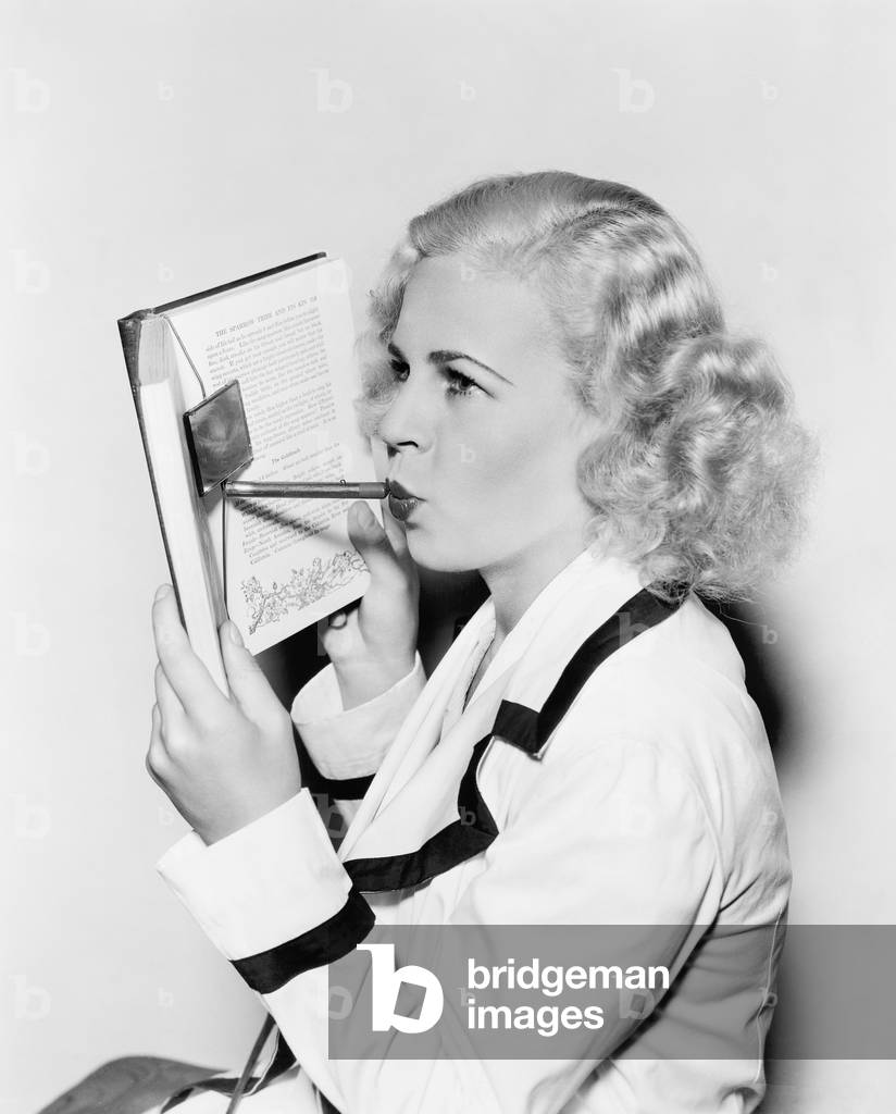 Young Woman Hiding her Face Behind a Book Applying Lipstick