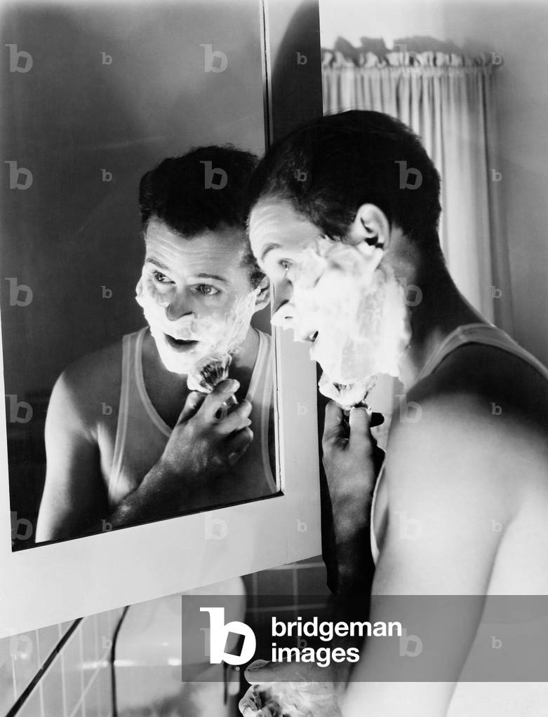Profile of a Young Man in Front of a Mirror in a Bathroom Shaving