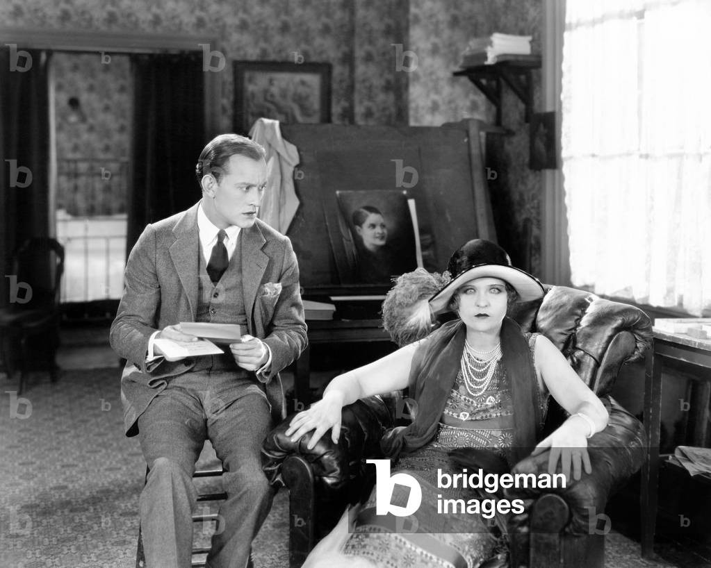 Man and Woman Sitting in a Living Room Reading a Letter and Looking Surprised
