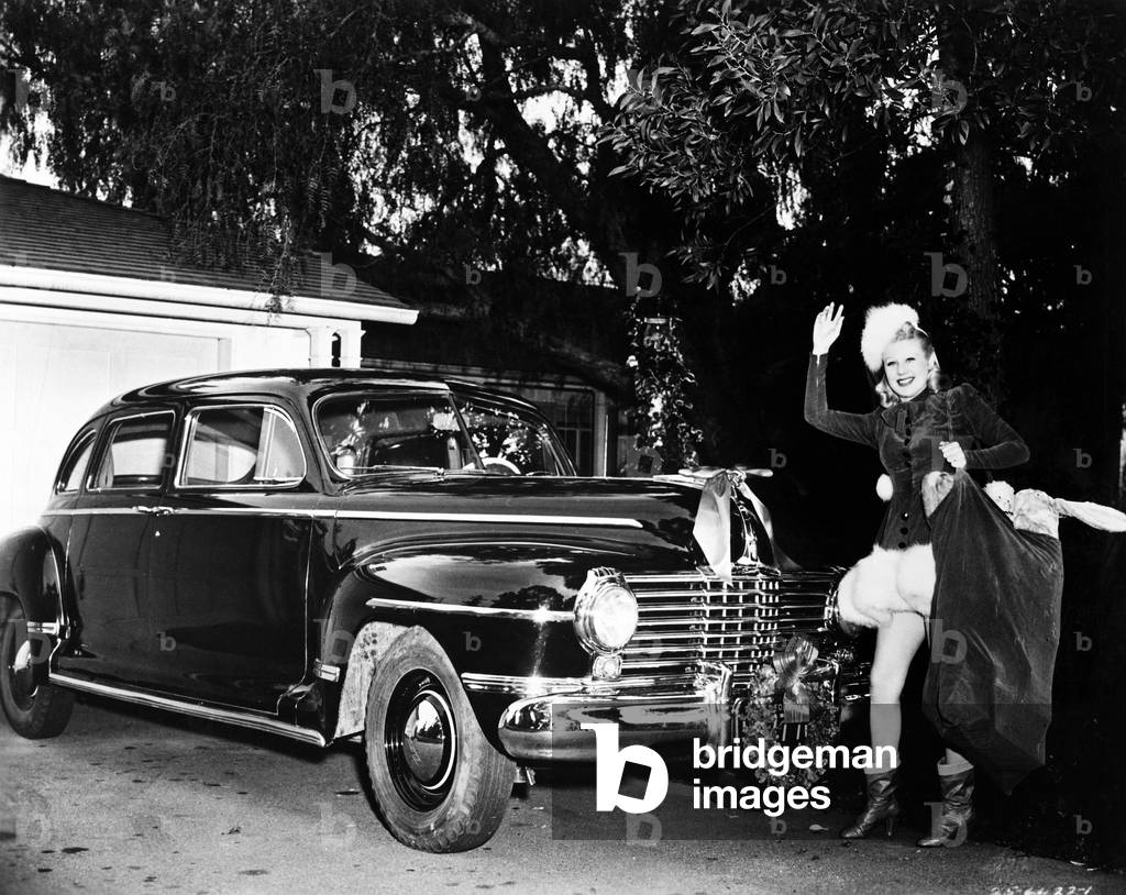 Woman Standing in Front of a Car Holding a Bag of Christmas Presents