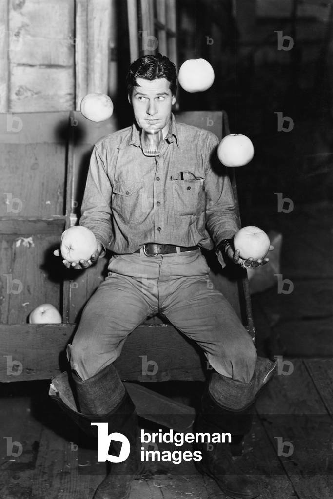 Young Man Juggling with Oranges and Balancing a Glass Under his Chin