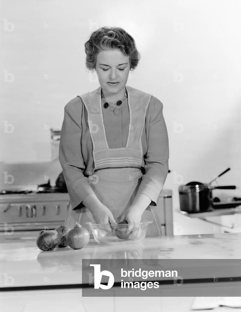 Woman Peeling Onions Into a Bowl in the Kitchen