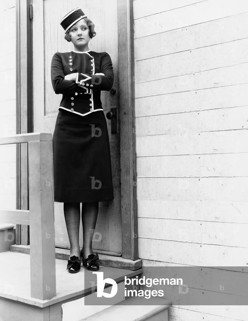 Young Woman in a Uniform Standing with her Arms Crossed in Front of a Closed Door