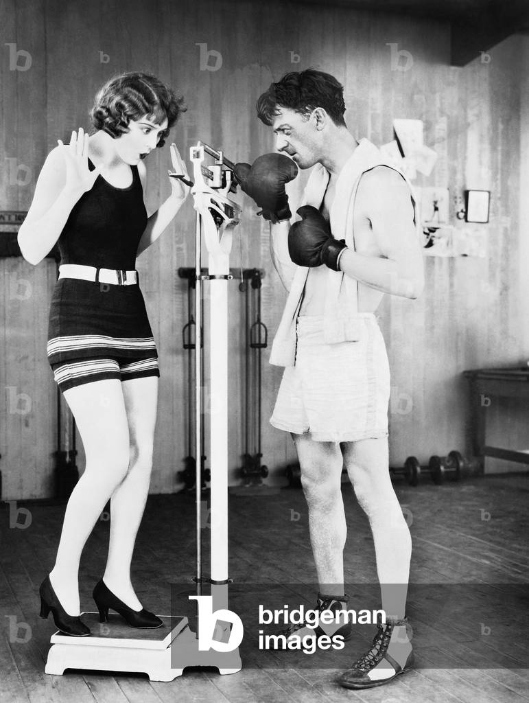 Young Woman Shocked at her Weight with a Man in Boxing Gloves