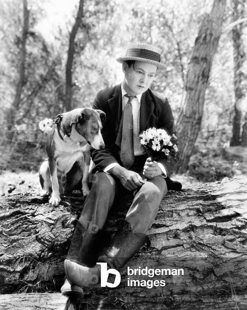 Young Man Sitting in the Woods with his Dog Looking Forlorn