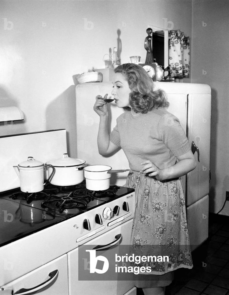 Young Woman in an Apron in her Kitchen Tasting her Food From a Pot