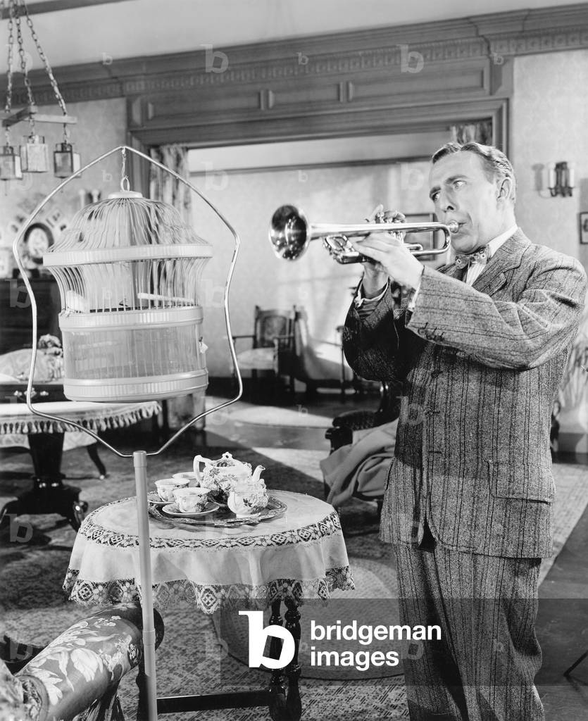 Man Standing in his Living Room Playing the Trumpet to a Bird