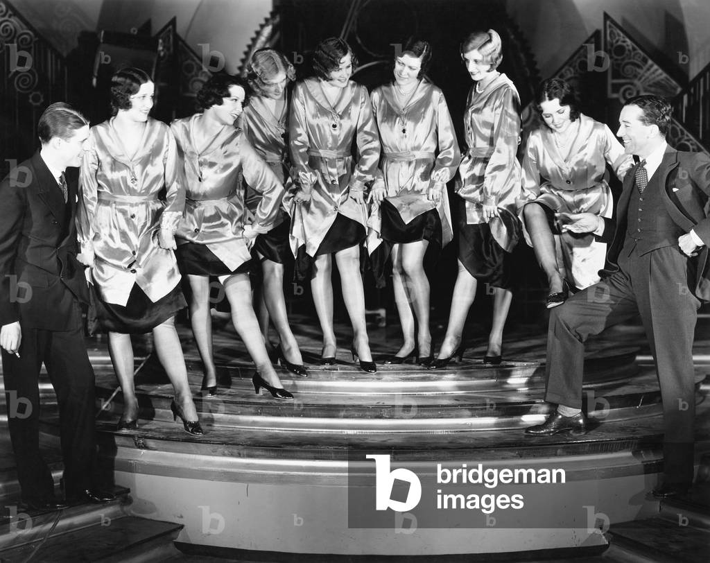A Chorus Line of Women Showing Off Their Legs to Two Men