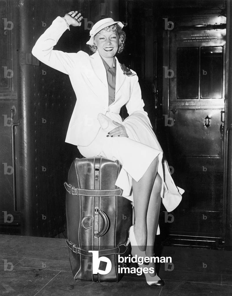 A Ready to Go Young Woman Sitting on her Suitcase and Waving